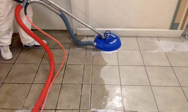 Tile and grout cleaning spinner crossing a visible cleaned and uncleaned boundary on a tiled floor